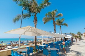 Relax in style with a clear view of the beach and sea from this outdoor seating area, complete with tables, chairs, and umbrellas.