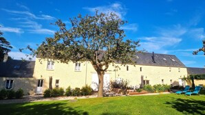 Un edificio de dos pisos con un gran árbol en el patio delantero, un césped cuidado y un cielo azul despejado.