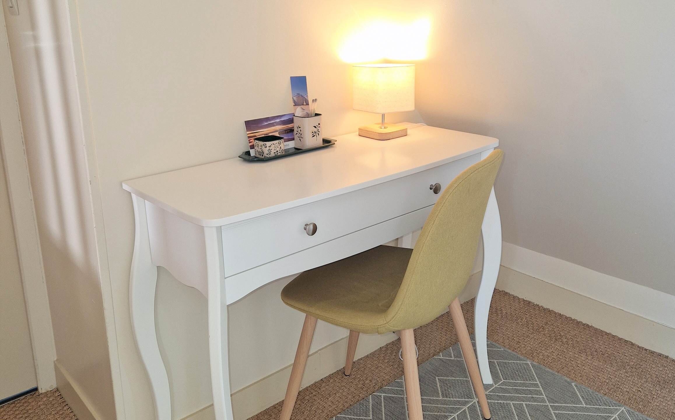 Een wit bureau met een lamp, een stoel en een klein doosje op het bureau.