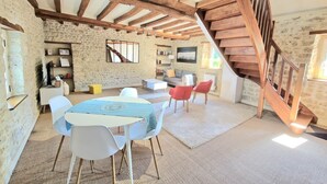 Un interior rústico con vigas de madera a la vista, pared de piedra, una escalera y un comedor con mesa y sillas.