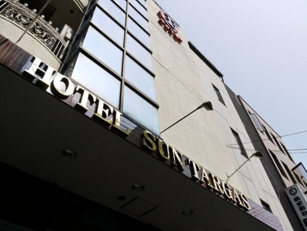 A hotel sign with the name 'HOTEL SUNTARGAS' and a reflection of a building facade.