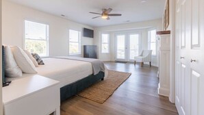 Ein geräumiges Schlafzimmer mit einem großen Bett, einem Deckenventilator und Blick ins Freie durch große Fenster.