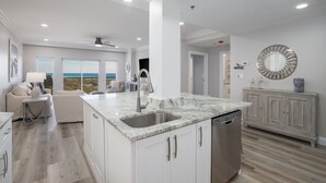 A modern kitchen with a large island, white cabinetry, and a view of the ocean. - Deja Blue, Gulf Views, Condo at Tops'l, Pool (Miramar Beach)