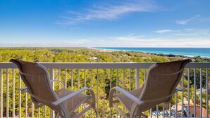 Two wicker chairs on a balcony overlooking a coastal landscape with a view of the sea and greenery. - Deja Blue, Gulf Views, Condo at Tops'l, Pool (Miramar Beach)