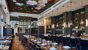 A restaurant with a long wooden table set for dining, hanging pendant lights, and a bar area with shelves of bottles. - Deja Blue, Gulf Views, Condo at Tops'l, Pool (Miramar Beach)