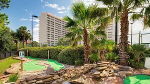 A mini-golf course with a pond, palm trees, and a building in the background. - Deja Blue Too Studio at Tops'l, Pool, Beach (Miramar Beach)