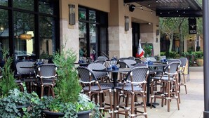 An outdoor dining area with tables and chairs, potted plants, and a building facade with large windows and outdoor lighting. - Deja Blue Too Studio at Tops'l, Pool, Beach (Miramar Beach)
