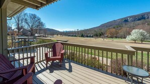 Une terrasse en bois, avec des chaises et une table, donnant sur un parc arboré et surmontée d’une montagne en arrière-plan.