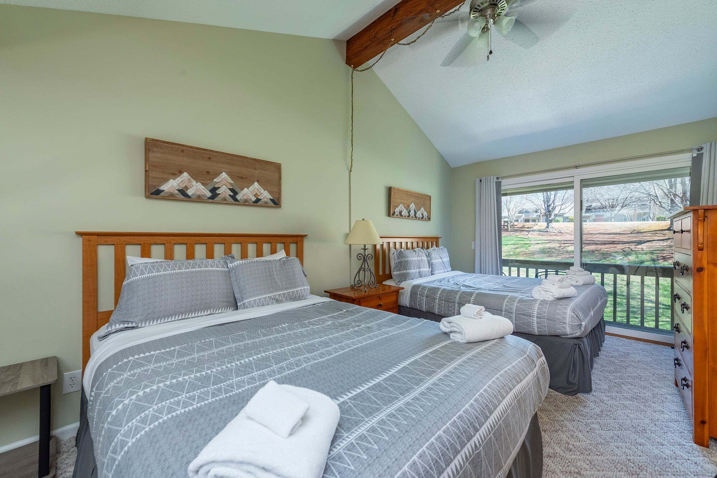 Une chambre avec deux lits, un ventilateur de plafond et une fenêtre donnant sur un beau paysage.