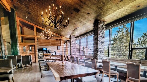 A spacious dining area with a long wooden table and benches, a chandelier, and large windows offering a view of the outdoors. - Experience Tahoe's Ski Scene at Holiday Inn Club Vacations Tahoe Ridge Resort (Stateline)