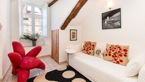 Une pièce chaleureuse avec un canapé blanc, un fauteuil rouge en velours, un tapis à motifs noir et blanc et une fenêtre donnant sur des immeubles.