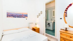 Une chambre à coucher comprenant un lit, une table de chevet, une lampe, un miroir et une vue sur le paysage urbain.