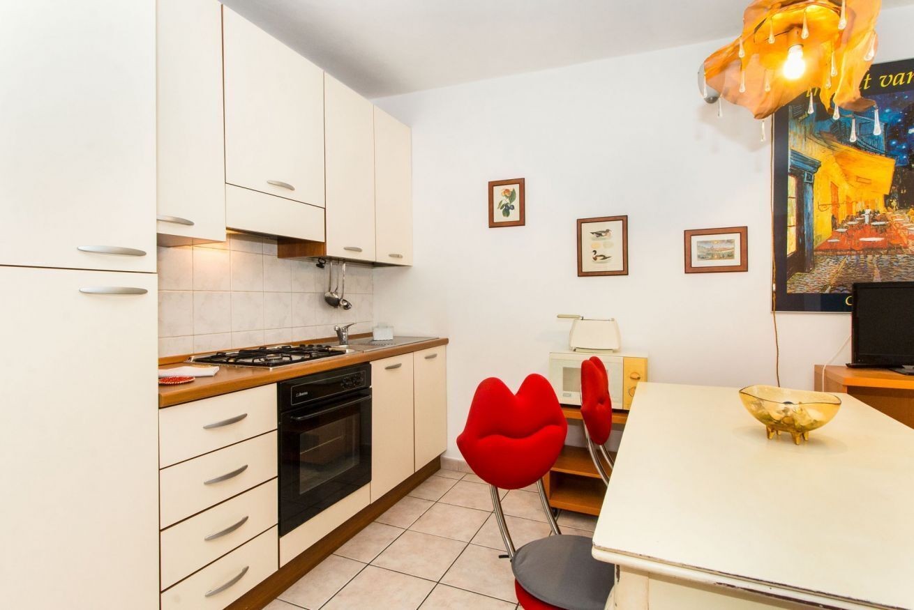 A modern kitchen with white cabinets, a stove, and a dining area with a white table and red chairs.