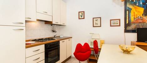 A modern kitchen with white cabinets, a stove, and a dining area with a white table and red chairs.