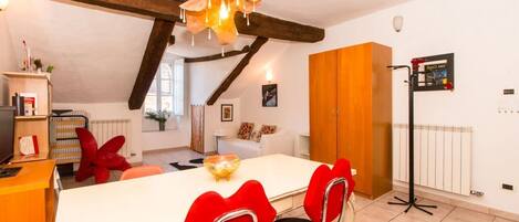 A dining area with a white table, red chairs, a chandelier, and wooden beams.