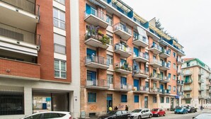 A multi-story residential building with balconies, a garage, and parked cars. - MM Pozzo Strada Terrace Apartment (Turin)