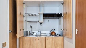 A compact kitchen with wooden cabinets, a stainless steel sink, a kettle, and a built-in range hood. - Porta Nuova & Valentino Apartment (Turin)