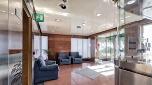 A modern lobby with a glass partition, two grey sofas, a potted plant, and a stainless steel elevator. - Porta Nuova & Valentino Apartment (Turin)