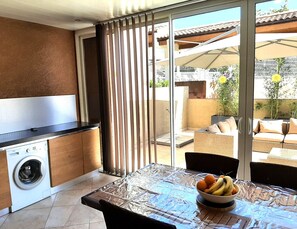 Una cocina con lavadora, una mesa de comedor con frutero y un ventanal corredero que da a una zona de estar exterior.