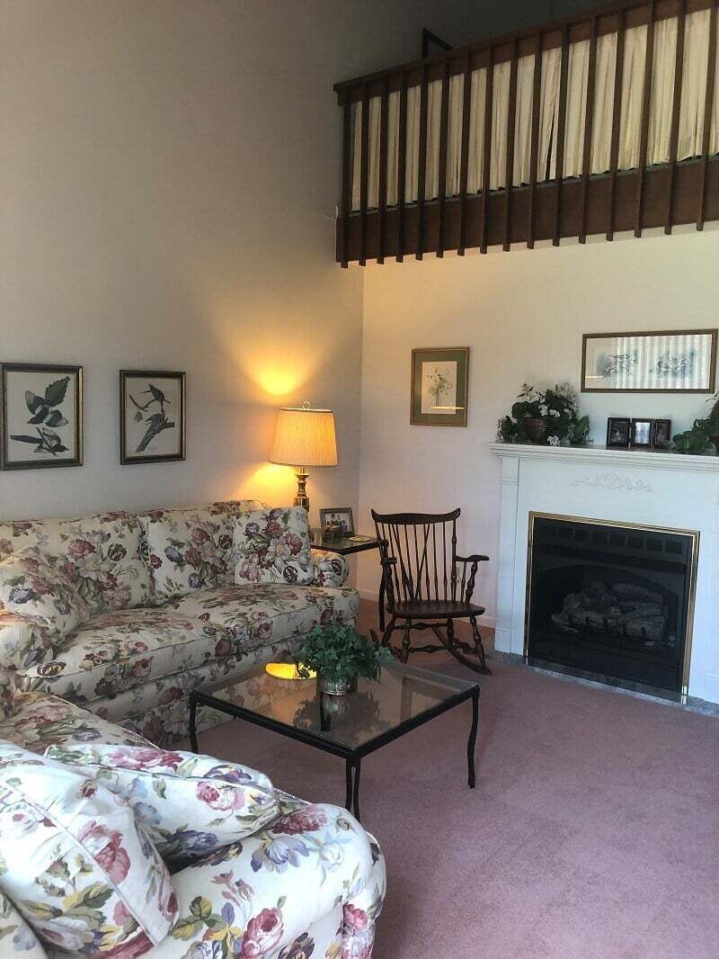 A living room with a sofa, a chair, a fireplace, and framed pictures on the wall.