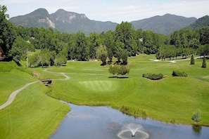 Un campo da golf con uno stagno, alberi e montagne sullo sfondo.