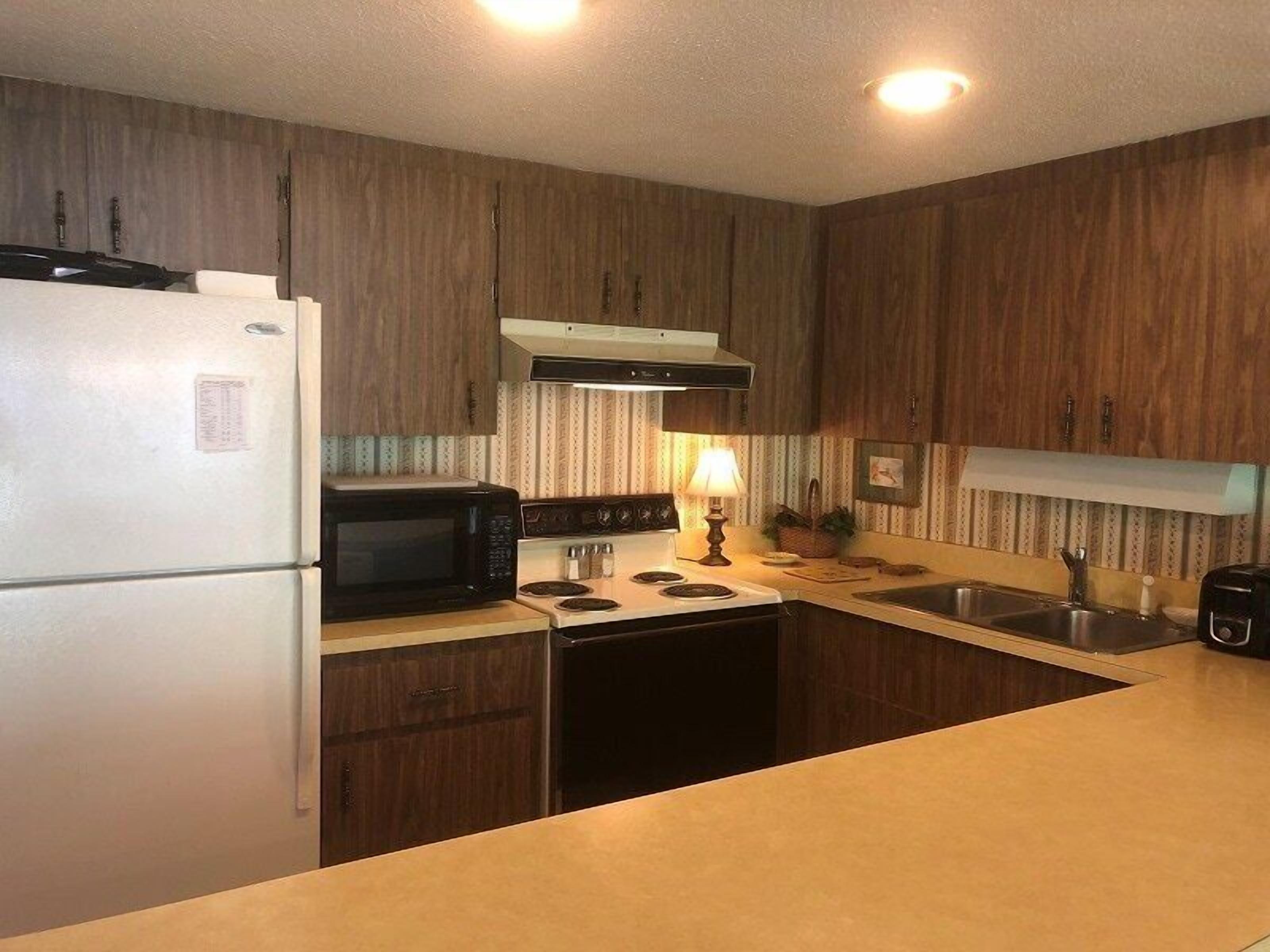A kitchen with wooden cabinets, a refrigerator, microwave, stove, and sink.