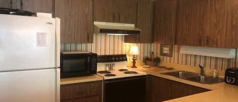 A kitchen with wooden cabinets, a refrigerator, microwave, stove, and sink.