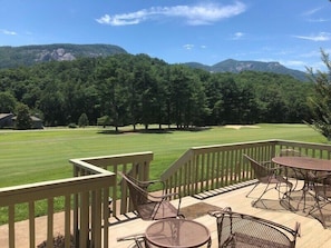 Una terrazza con mobili da esterno che si affaccia su un campo da golf e montagne boscose.