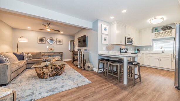 A modern living room with a sectional sofa, a coffee table, and a TV. The kitchen features white cabinets, a bar area, and a refrigerator. -  5 star condo on Main Street! (Dunedin)