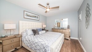 A bedroom with a bed, nightstands, a dresser, a ceiling fan, a mirror, and a wall-mounted light switch. -  5 star condo on Main Street! (Dunedin)