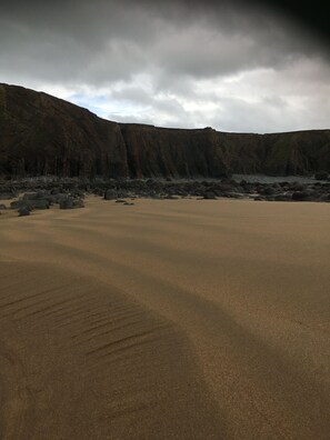 A beach with large rocks and a cliff in the background.
