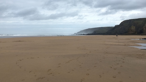 A wide sandy beach with footprints, a distant view of the ocean, and a rocky cliff in the background. - Lovely 3 Bedroom Holiday Bungalow Near Bude (Bude)