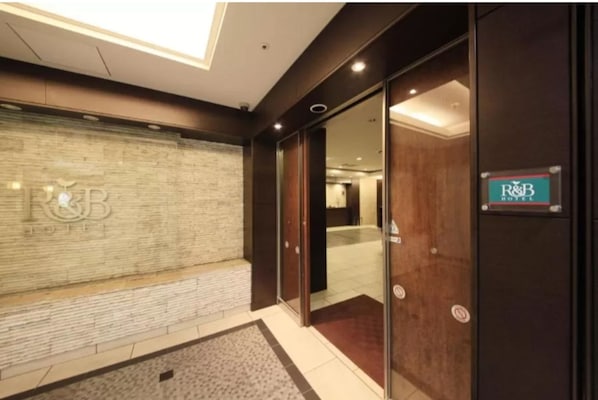 A hotel entrance with a glass door, a sign for R&B Hotel, and a textured wall.