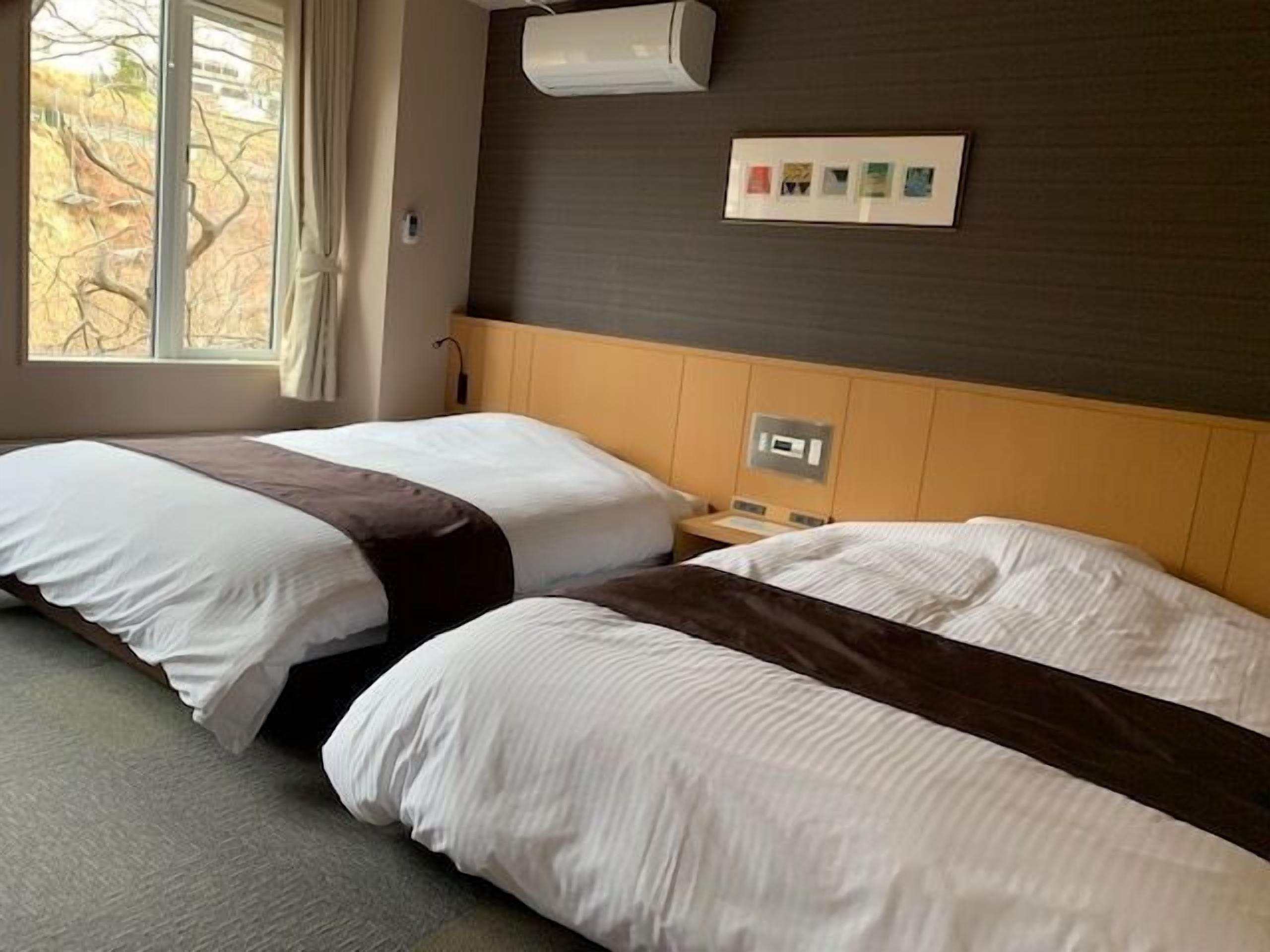 Habitación de hotel con dos camas, una ventana, un equipo de aire acondicionado y un panel de control en la pared.