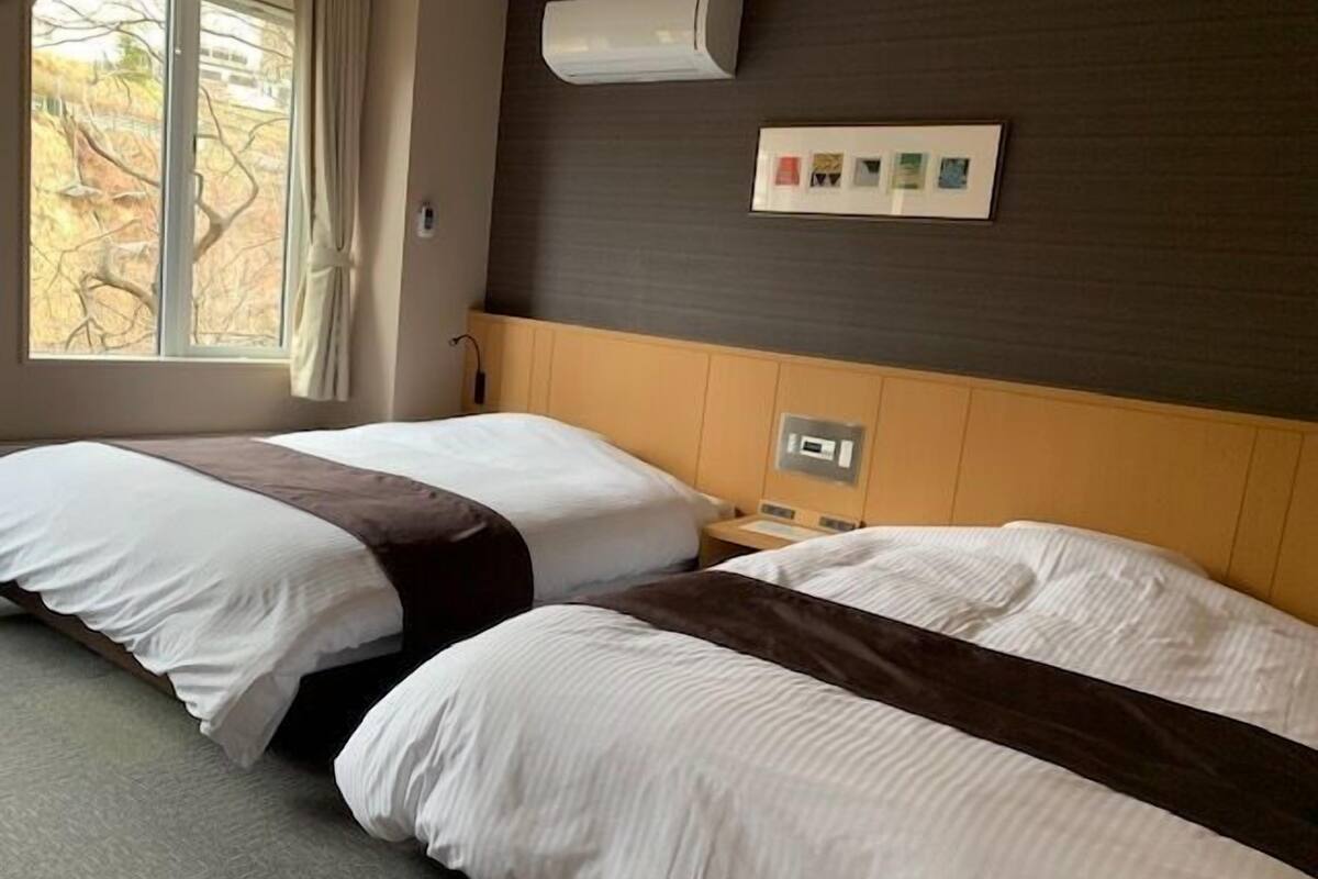 Een hotelkamer met twee bedden, een raam, een airconditioningsysteem en een bedieningspaneel aan de muur.