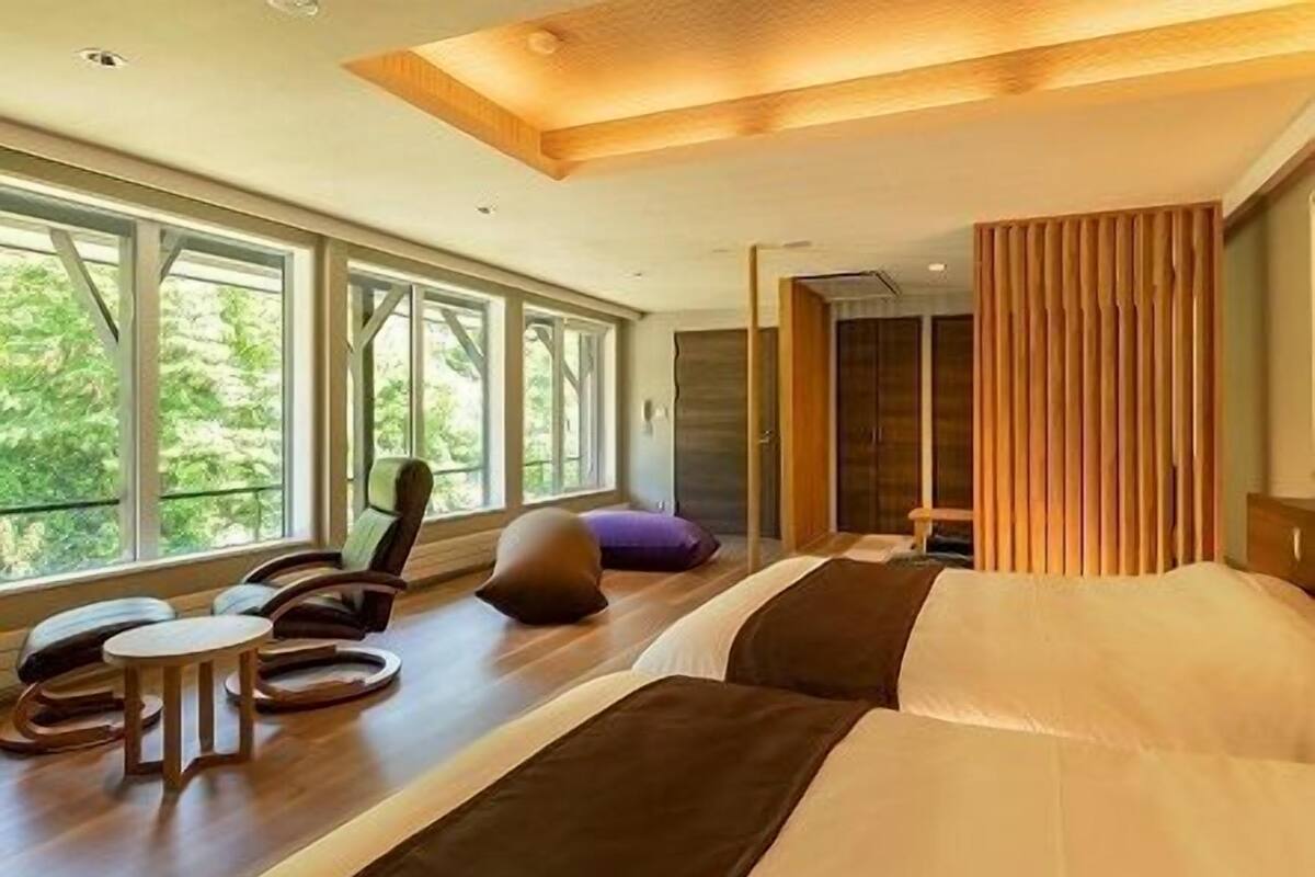 Een moderne hotelkamer met grote ramen, een bed, een zithoek met een stoel en een klein tafeltje, en een kledingkast.