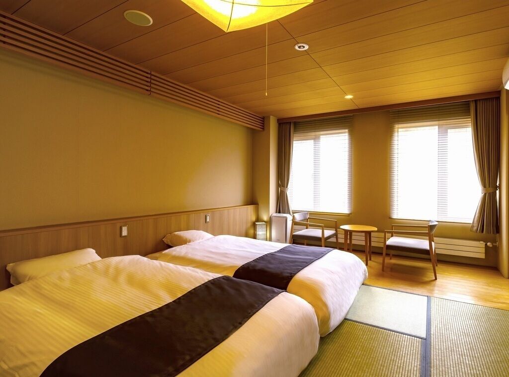 Habitación de hotel con dos camas, una mesita, sillas y una ventana con cortinas.