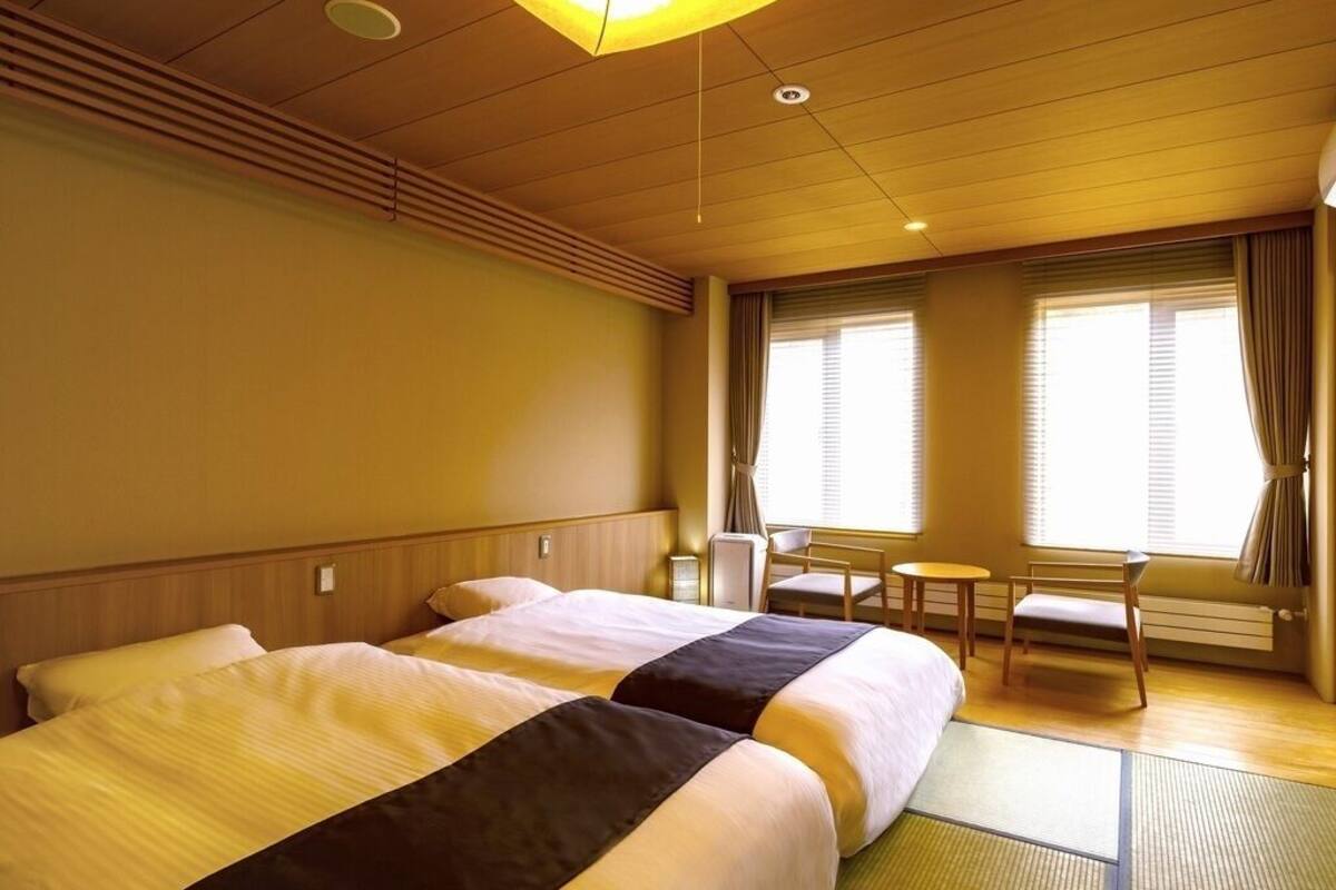 Een hotelkamer met twee bedden, een tafeltje, stoelen en een raam met gordijnen.