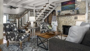 A spacious living room with a fireplace, a staircase, and a large painting on the wall. - 1800’s Home at Lost Creek/Hot Tub/Close to Downtown/Bluebonnet (Fredericksburg)