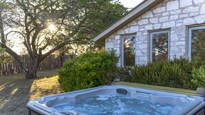 A hot tub in front of a stone house with a wooden fence and a tree. - 1800’s Home at Lost Creek/Hot Tub/Close to Downtown/Bluebonnet (Fredericksburg)