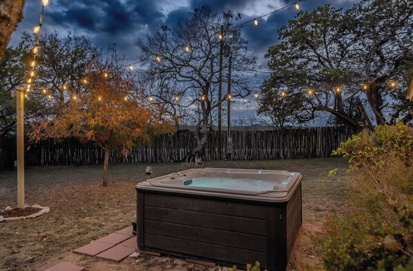 A hot tub in a backyard with string lights and trees.