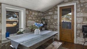 A rustic room with a stone wall, a wooden door, a bench, and a table with a vase of flowers. - 1800’s Home at Lost Creek/Hot Tub/Close to Downtown/Bluebonnet (Fredericksburg)