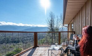 Un balcón con vista a las montañas, una mesa con sillas y una persona leyendo un libro.