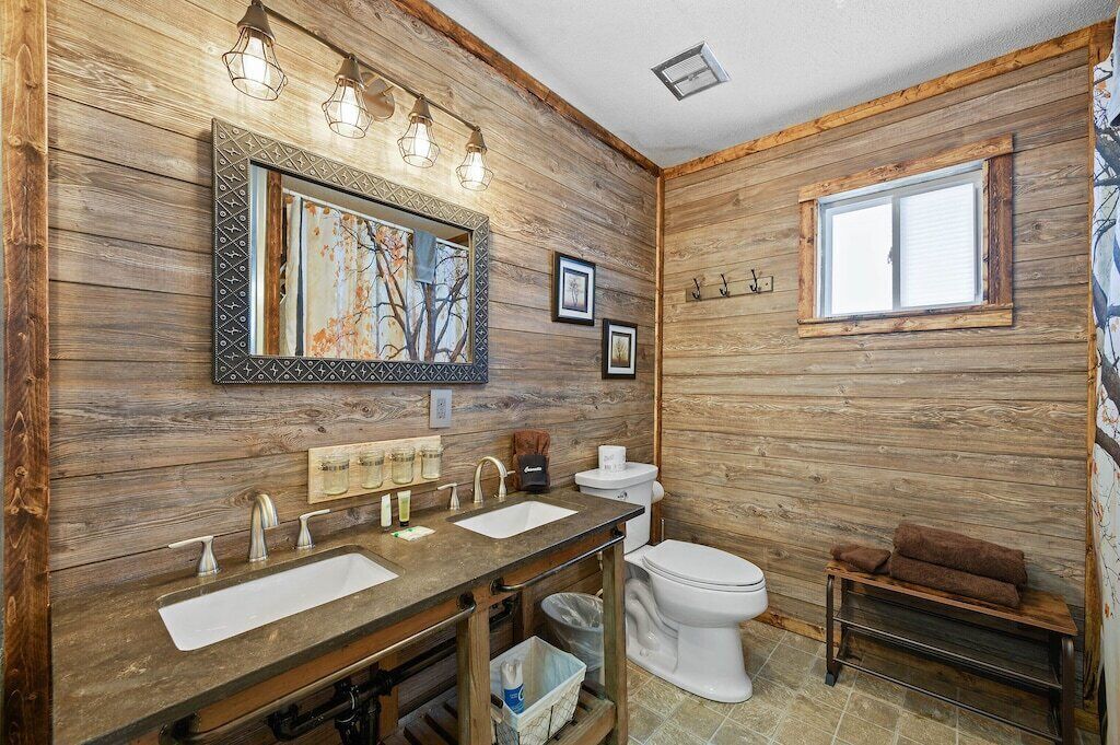 Une salle de bain rustique avec des murs en bois, un grand miroir et une fenêtre.