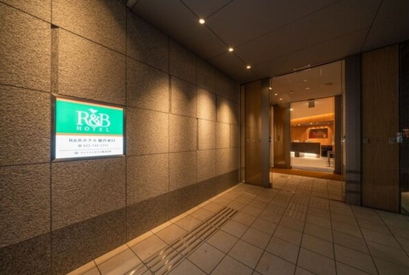 A hotel entrance with a sign for R&B Hotel, a tiled floor, and a doorway leading inside.