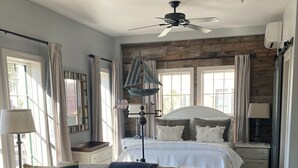 Un dormitorio acogedor con cama, mesitas de noche, ventilador de techo y ventana con cortinas.