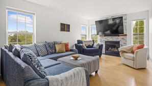 A spacious living room with a large sectional sofa, a fireplace, and a flat-screen TV mounted above it.