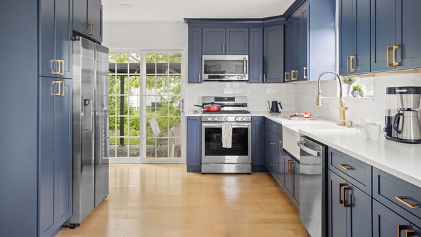 A modern kitchen with dark blue cabinets, stainless steel appliances, and a large window.