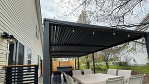 Une terrasse extérieure dotée d’un espace salon couvert, d’une table avec des chaises et d’un barbecue.
