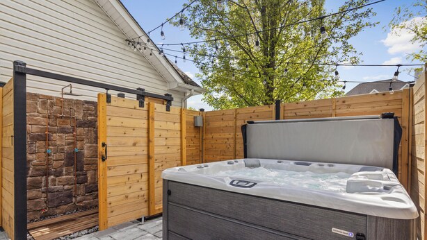 Un bain à remous dans un jardin, avec un mur en pierre, une clôture en bois et un arbre.